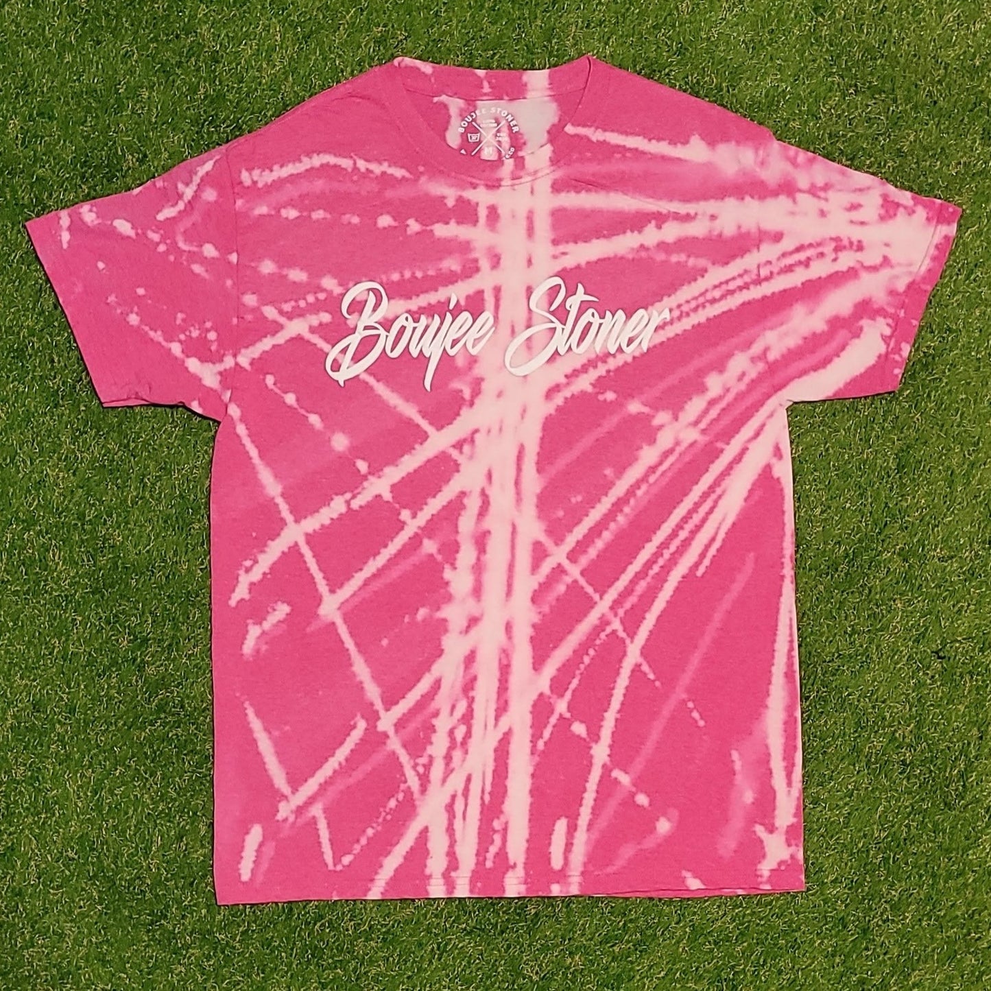Boujee Stoner Bleached Tee in a soft pink "Rose Quartz" color with a bold white bleach design, displayed on a green grassy background.