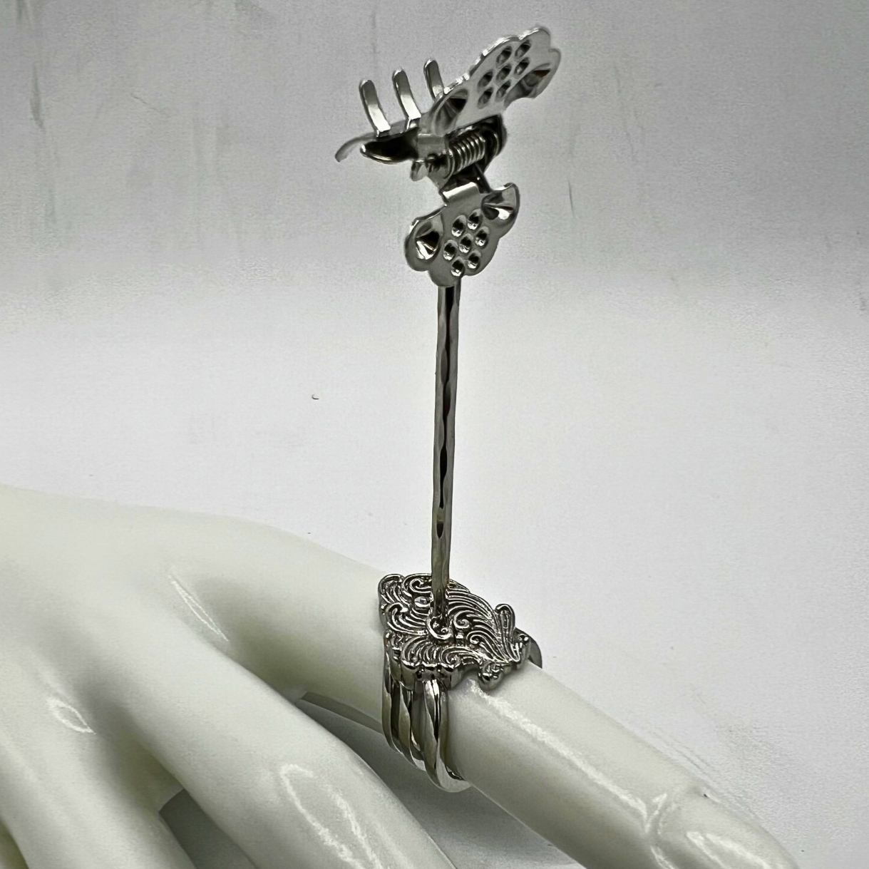 Silver ring with decorative design on a white mannequin hand against a white background