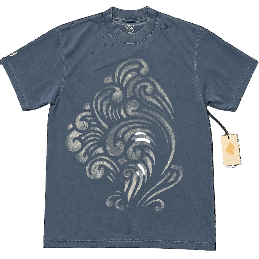 A washed slate blue short-sleeve t-shirt with a distressed white graphic print of a stylized wave or bird design on the front. The shirt is displayed flat against a white background with a paper hangtag attached to the right sleeve.