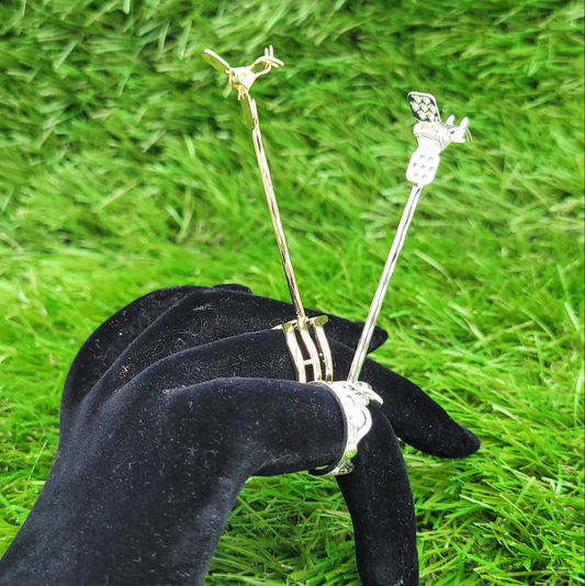 A gold and a silver Boujee Stoner Ring with joint clips, worn on a black velvet hand against a backdrop of green grass.