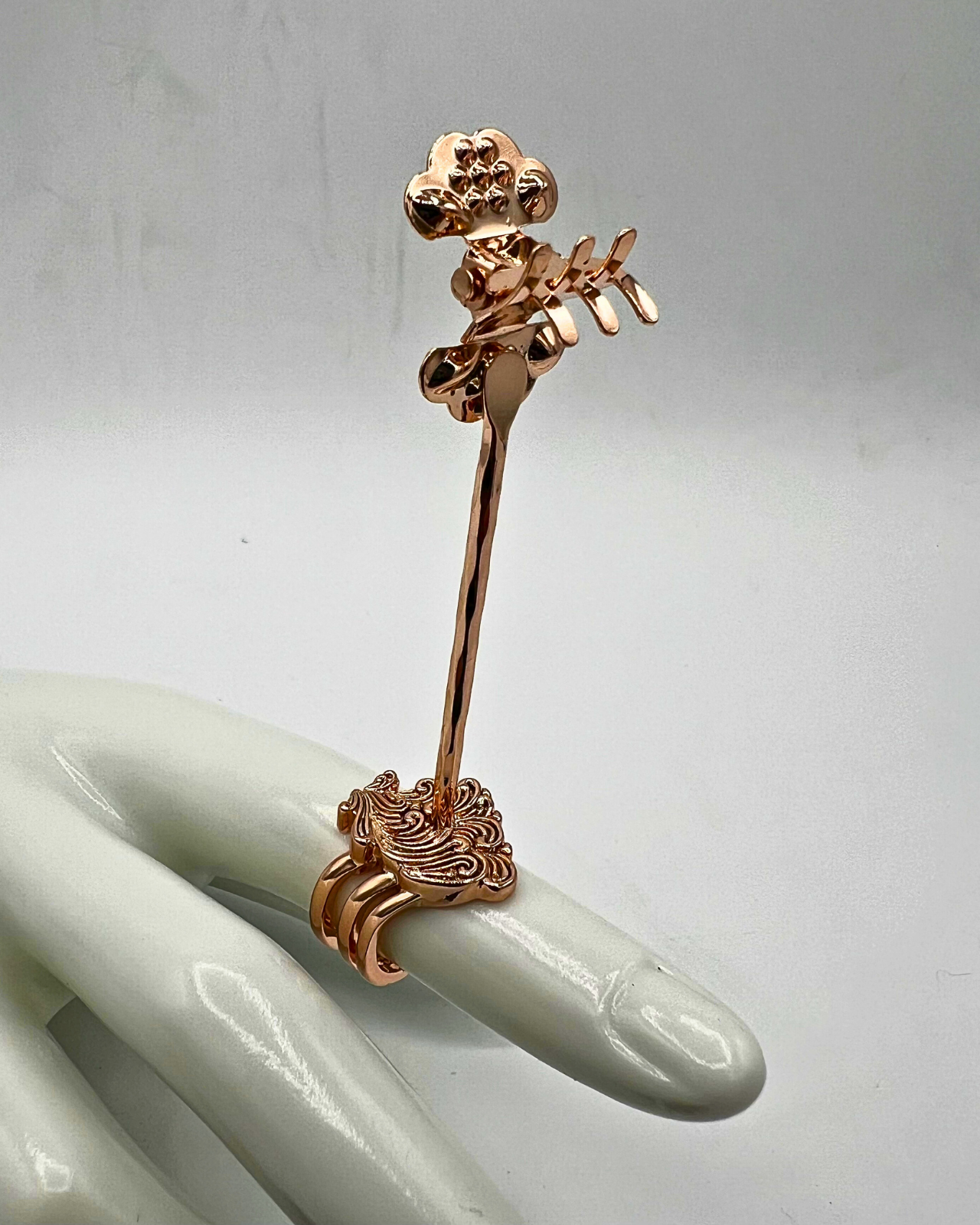 Rose gold decorative ring on a mannequin hand against a light gray background